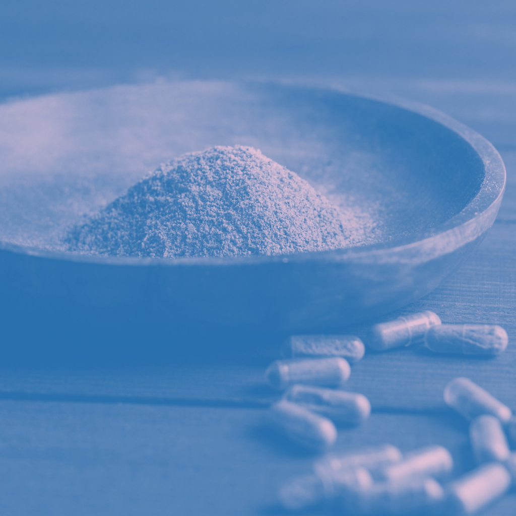 A pile of Kratom powder on a plate with a pile of Kratom filled capsules next to it.